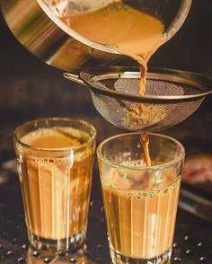 two shot glasses filled with liquid and being poured into them by a strainer on the side