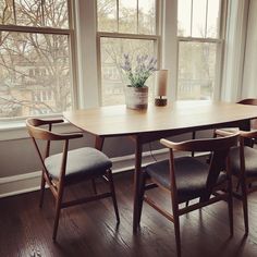 a wooden table with four chairs and a potted plant in the window sill