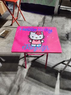 a pink hello kitty table sitting on top of a carpeted floor next to two red chairs