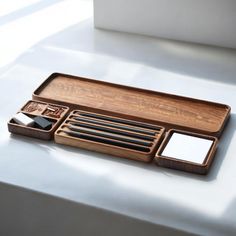 a wooden tray with various items in it on a white tableclothed surface and sunlight coming through the window