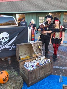 two women dressed in pirate costumes standing next to a trunk filled with candy and other items