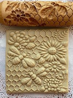 a piece of carved wood with flowers and bees on it next to a rolling pin