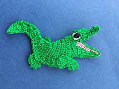 a green crocheted alligator brooch sitting on top of a blue surface