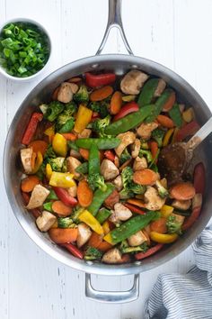 a pan filled with chicken and veggies next to a small bowl of greens