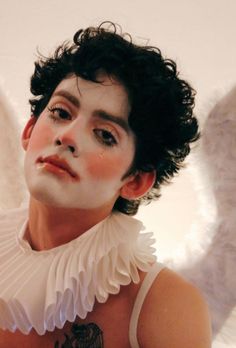 a woman with white wings on her chest and black hair is posing for the camera