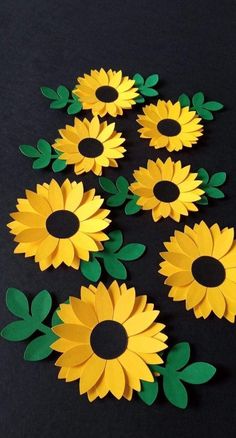 paper sunflowers with green leaves are arranged on a black surface, in the shape of circles