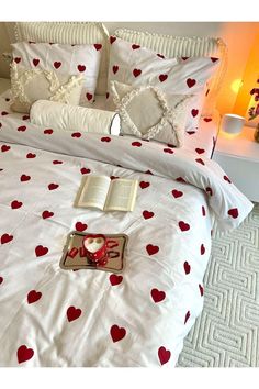 a bed with red hearts on it and an open book sitting on the pillow next to it