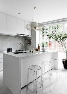 a kitchen with white cabinets and stools next to a plant in a pot on the counter