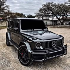 a black mercedes g - class is parked in the gravel