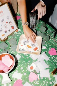 two people are cutting hearts out of paper on a table with other decorations and papers