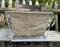 a chicken wire basket sitting on top of a wooden bench next to a garden fence