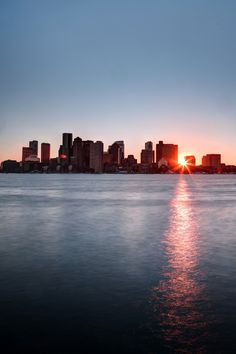 the sun is setting in front of a cityscape with water reflecting off it's surface