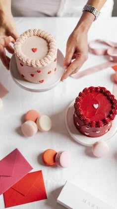 a woman decorating a cake with red icing and hearts on the frosting