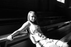 a woman sitting on top of a wooden bench next to a bleachers window