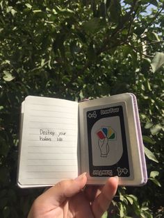 an open book with writing on it in front of some trees and bushes that are green