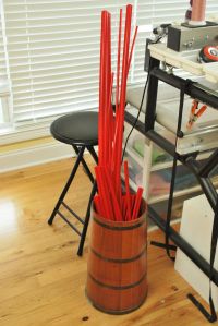 a wooden table topped with lots of clutter next to a metal rack filled with red sticks