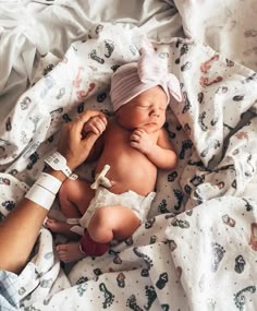 a baby laying on top of a bed next to a person wearing a white headband