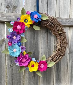 a wreath made out of felt flowers sitting on top of a wooden fence next to a pole