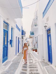 a woman walking down an alley way in the middle of white buildings with blue doors