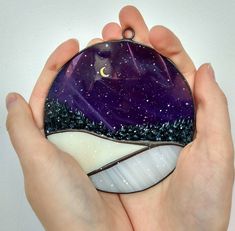 a hand holding a purple and white glass ornament with a crescent on it