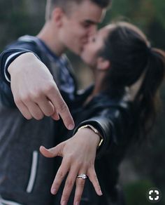 a young man and woman are kissing with their fingers pointing at the camera while holding each other's hand