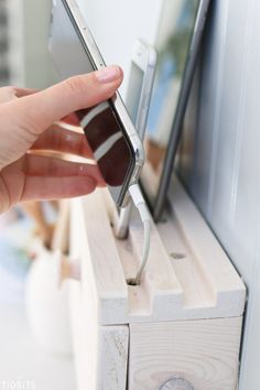 a hand holding a cell phone in front of a mirror on a wooden shelf next to a window