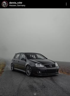 a black car parked on the side of a road in front of a foggy sky