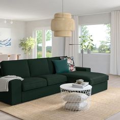 a living room with a green couch and white table in the middle, surrounded by large windows