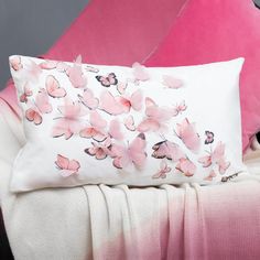 a white pillow with pink flowers on it sitting on a chair next to a blanket