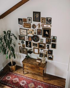 a room with many framed pictures on the wall next to a wooden table and potted plant