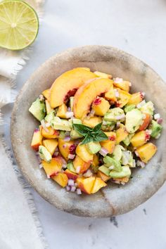 a bowl filled with fruit and vegetables on top of a white cloth next to an avocado