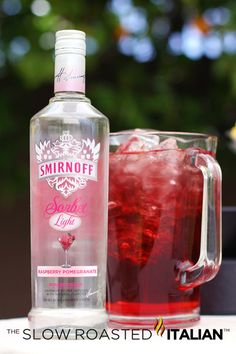 a bottle of vodka next to a glass filled with ice and red liquid on a table