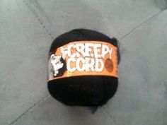 a black hat with an orange band that says keep the cord attached to it, sitting on top of a gray surface