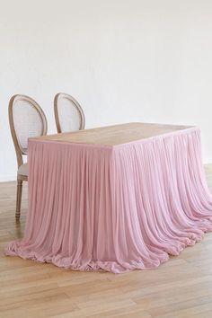 a table with two chairs and a pink cloth draped over it in front of a white wall