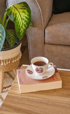 a cup of coffee sitting on top of a table next to a book and potted plant