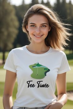 a woman wearing a white tee shirt with the words fee time on it and a golf course in the background