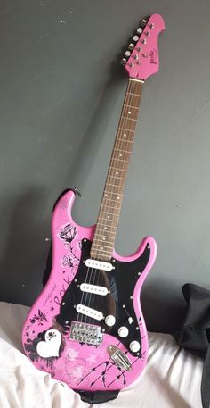 a pink and black guitar sitting on top of a white bed next to a wall