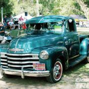 an old green truck is parked in the grass with people standing around and looking at it