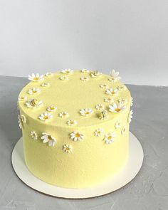 a yellow cake with white daisies on the top is sitting on a gray surface