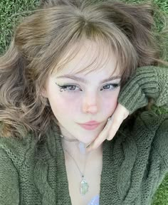 a woman laying in the grass with her hand on her head and looking at the camera