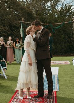 a bride and groom kissing on a rug in front of an outdoor ceremony with guests