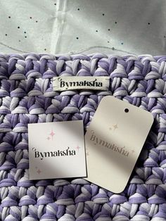 two tags that are sitting on top of a purple and white knitted blanket,