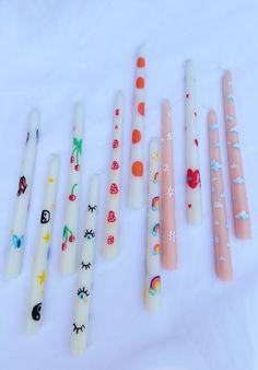 five different colored candles are lined up on a white tablecloth, with designs painted on them