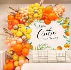 an orange and yellow wedding arch with chairs in front of the sign that says, a little quietie is on the way