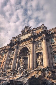 an ornate building with statues on the front and side walls, against a cloudy sky