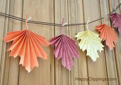 three different colored paper leaves hanging from a line on a wooden surface with clothes pins