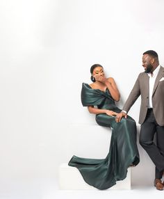 a man standing next to a woman in a long green dress on a white surface