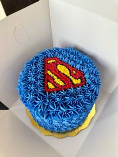 a blue and yellow cake with a superman symbol on it's top in a box