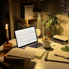 an open laptop computer sitting on top of a wooden table next to books and candles