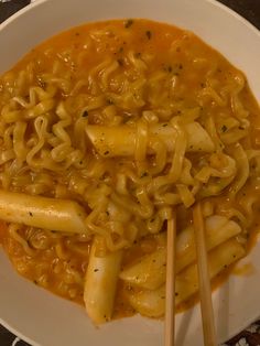 a white bowl filled with noodles and cheese on top of a table next to chopsticks